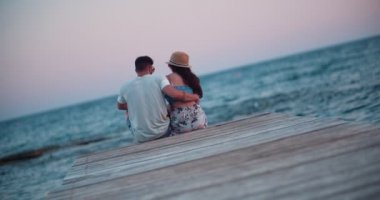 Ahşap iskelede oturan romantik çift öpüşüyor.