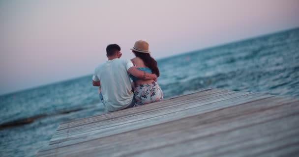 Jovem casal romântico beijando enquanto sentado no molhe de madeira — Vídeo de Stock