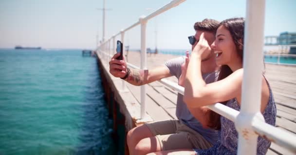 Happy young hipster couple video-chatting using smartphone on wooden pier — Stock Video