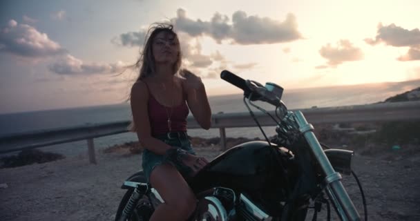 Hermosa mujer motociclista rubia bajándose de la motocicleta al atardecer — Vídeo de stock