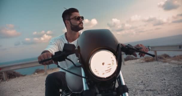 Joven macho con tatuajes en motocicleta mirando el atardecer — Vídeos de Stock