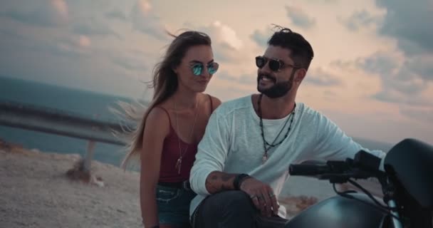 Młody macho mężczyzna i dziewczyna siedzi na motocyklu o zachodzie słońca — Wideo stockowe
