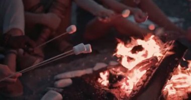 Çok ırklı erkek ve kadınlar kamp ateşinde lokum kızartıyorlar.