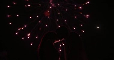 Geceleri havai fişek gösterisi altında öpüşen genç çift.