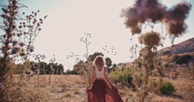 Genç hippi kadın sonbaharda kır çiçeklerinin arasında yürüyor.