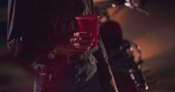 Jovem motociclista mulher segurando copo de plástico no festival de música noturna — Vídeo de Stock