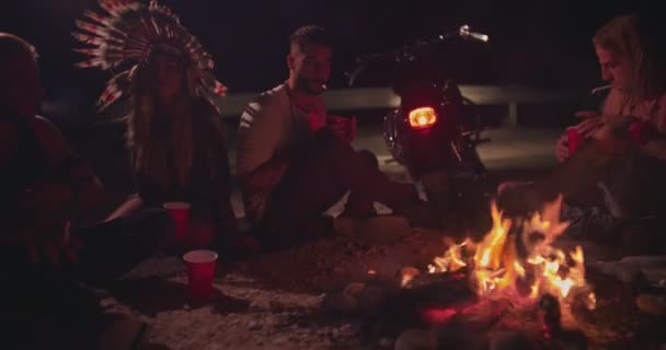 Genç asi motosikletçi arkadaşlar kamp ateşinin etrafında sigara ve içki içiyorlar. — Stok video
