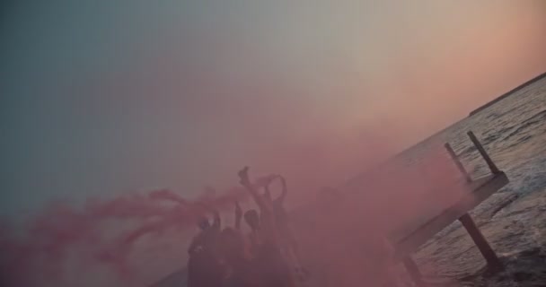 Amigos multiétnicos celebrando con bombas de humo en embarcadero al atardecer — Vídeo de stock