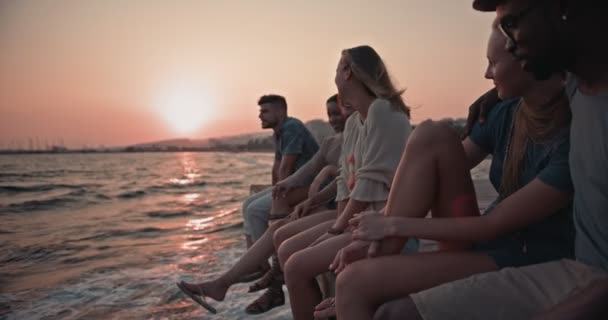 Młodzi, wieloetniczni przyjaciele i pary relaksujące się na molo o zachodzie słońca — Wideo stockowe