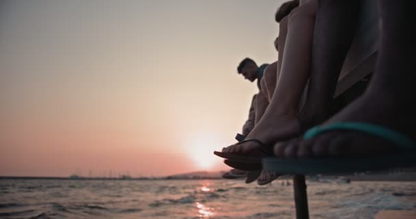 Multi-ethnic friends sitting on pier with their legs hanging down — Stock Video