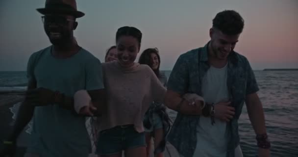 Молоді багатоетнічні друзі-хіпстери ходять по дерев'яному пірсу на заході сонця — стокове відео