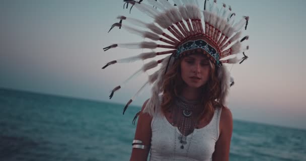 Boheemse vrouw met inheemse Amerikaanse veren hoofdtooi op het strand — Stockvideo