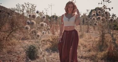 Sonbahar kır çiçekleri tarlasında yürüyen boho tarzı genç bir kadın.
