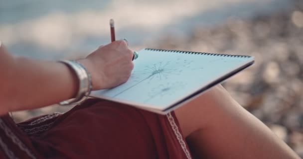 Mujer en estilo boho dibujando en cuaderno de bocetos en la playa — Vídeo de stock