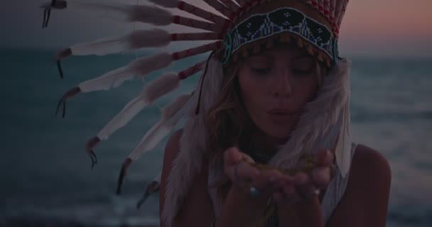 Femme hippie avec coiffe en plumes soufflant des paillettes à la plage — Video