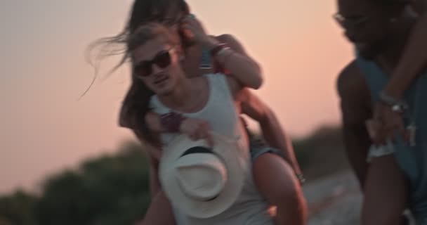 Młode wieloetniczne pary na plaży na wyspie uprawiają jazdę na barana — Wideo stockowe