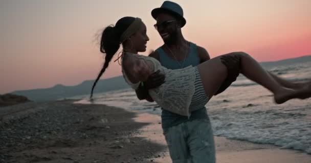 Novio romántico llevando y girando novia en la playa al atardecer — Vídeo de stock