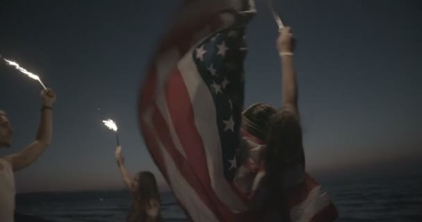 Multi-ethnic friends partying on beach with sparklers and American flag — Stock Video
