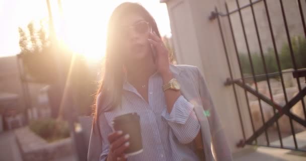 Jonge zakenvrouw met koffie praten aan de telefoon buiten — Stockvideo