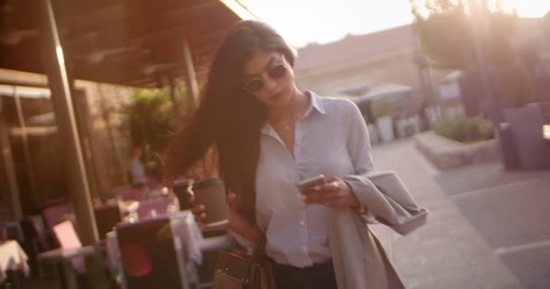 Joven mujer de negocios con café caminando y mensajes de texto en la ciudad — Vídeo de stock