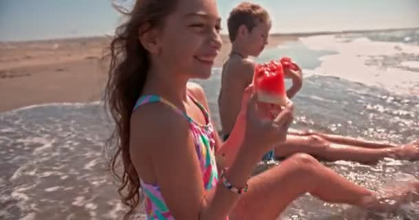 Fiatal fiú és lány eszik görögdinnyét a strandon — Stock videók