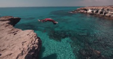 Genç uçurum dalgıcı takla atarak kayadan denize atlıyor.