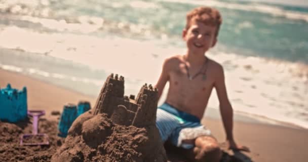 Jonge lachende jongen bouwen zandkastelen op het strand in de zomer — Stockvideo