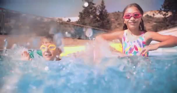 Gutt og jente som har det gøy plasker vann i svømmebasseng – stockvideo