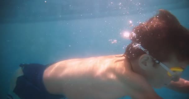 Niño con gafas nadando bajo el agua en la piscina — Vídeo de stock