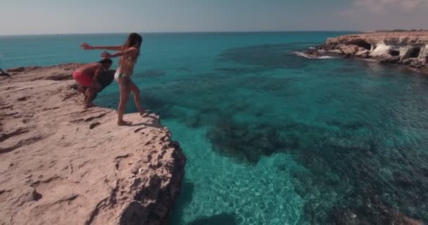 Young divers couple jumping off cliff into the ocean — Stock Video