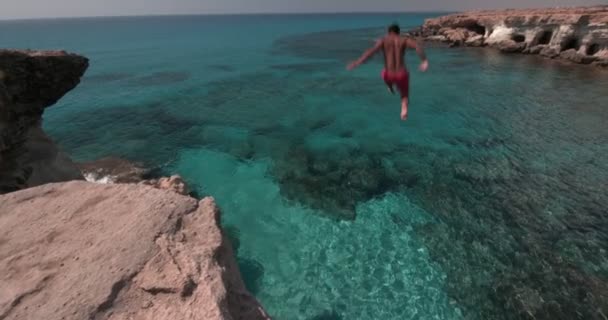 Молодой человек прыгает со скалы и ныряет в море — стоковое видео