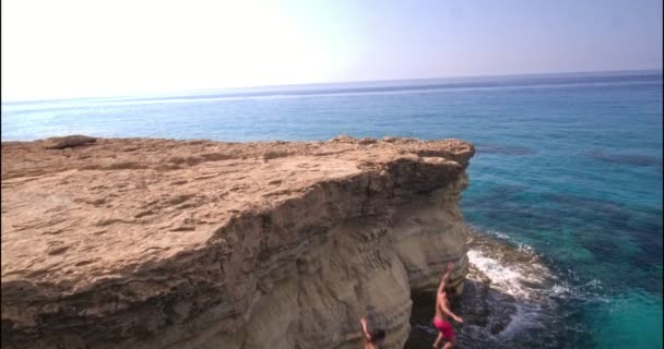 Aerial view of couple jumping off cliff into the ocean — Stock Video