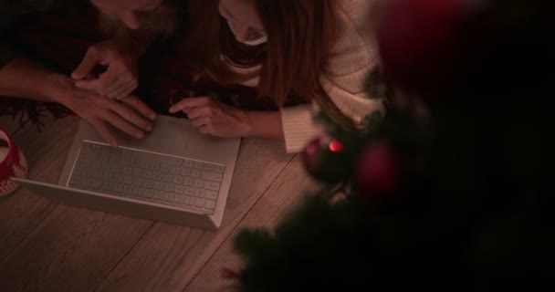 クリスマスツリーの下でオンラインショッピングのためのラップトップを使用してカップルをRedhead — ストック動画