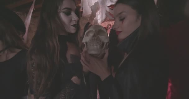 Молодые женщины в страшных костюмах облизывают череп на вечеринке Хэллоуина — стоковое видео