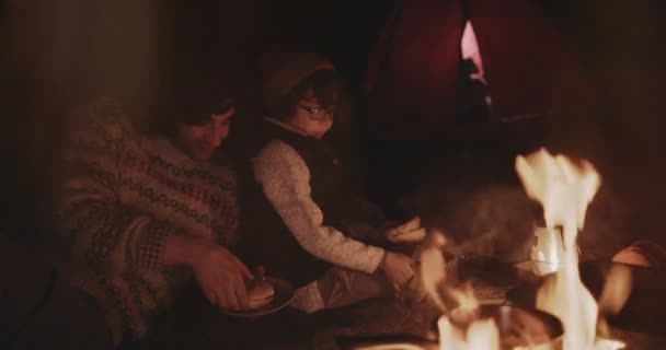 Jonge vader en zoon kampeerders eten 's nachts rond kampvuur — Stockvideo