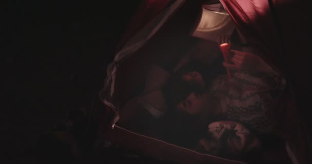 Отец и сын читают книги в палатке для кемпинга ночью — стоковое видео