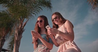 Hipster ergen en iyi arkadaşlar Palm Tree plajında mesajlaşıyorlar.