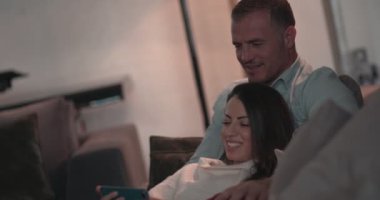 Çift evde dinlenirken akıllı telefon kullanıyor ve video izliyor.