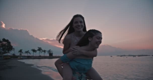 Hipster teenager girls having fun mit huckepack ride on beach — Stockvideo