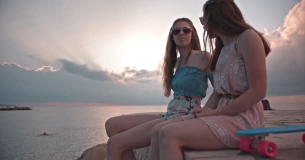 Adolescentes con patinetas sentadas junto al mar al atardecer — Vídeos de Stock