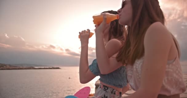 Молоді жінки-хіпстери зі скейтбордами п'ють соду на пляжі — стокове відео