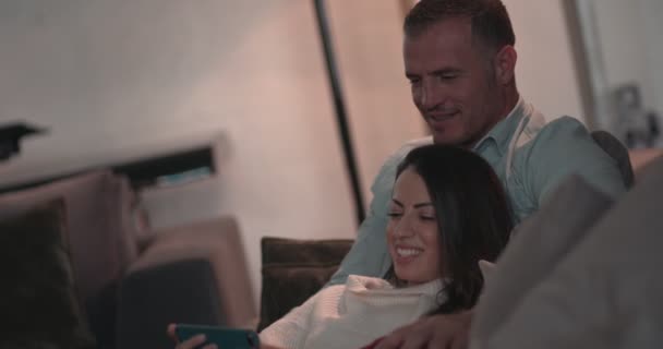 Ζευγάρι που χρησιμοποιεί smartphone και παρακολουθεί βίντεο ενώ χαλαρώνει στο σπίτι — Αρχείο Βίντεο