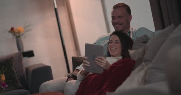 Зрелая шикарная пара, пользующаяся планшетом и развлекающаяся дома — стоковое видео