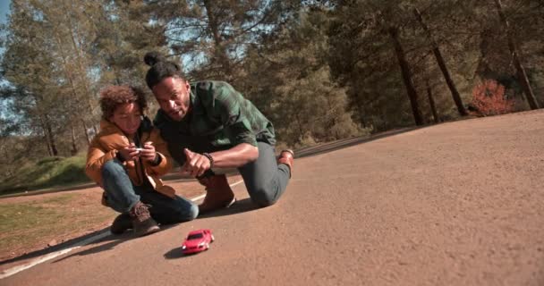 Otec a syn si hrají s dálkově ovládaným autem v parku — Stock video