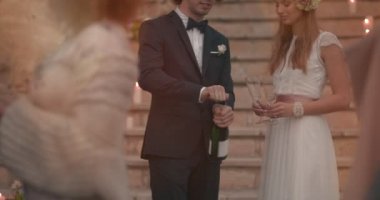 Yeni evli gelin ve damat kutlama yapıyor ve şampanya şişesi açıyor.