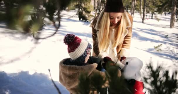 Joven madre e hijo haciendo muñeco de nieve en el bosque nevado — Vídeos de Stock