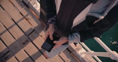 Rıhtımda kaykaylı genç adam cep telefonuyla mesajlaşıyor.