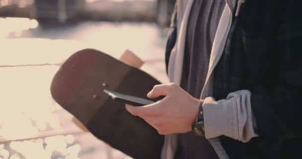 Hipster adolescente skate mensajes de texto y caminar en embarcadero — Vídeo de stock