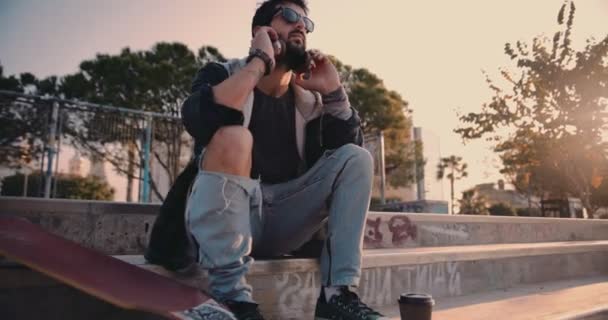 Jeune skateboarder avec écouteurs et café relaxant au skateboard park — Video