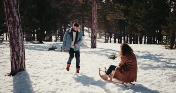 Novio tirando novia en trineo en snowy forest park — Vídeo de stock